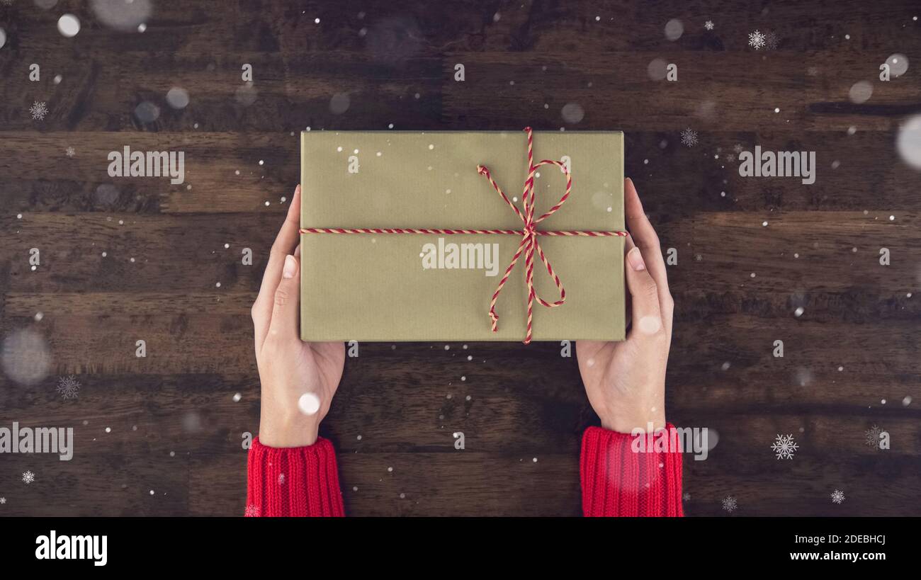 Frau Hände geben christsmas Geschenkbox Draufsicht auf Holz Tischhintergrund mit Schnee` Stockfoto